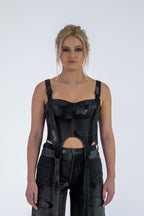 Woman wearing a black sleeveless top with cut-out design and high-waisted pants on a white background