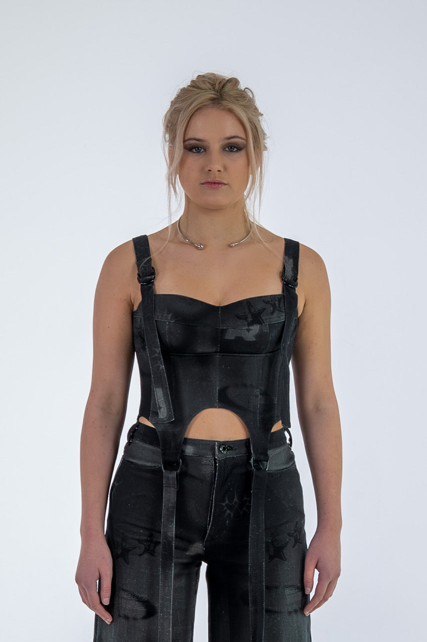 Woman wearing a black sleeveless top with cut-out design and high-waisted pants on a white background
