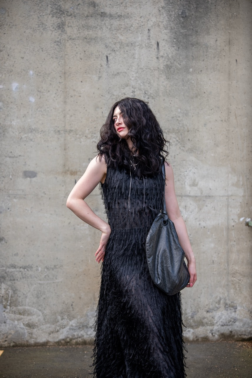 Person wearing a black sleeveless dress with fray details handmade by Rhian in Dunedin on a textured wall