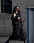 Woman in a black textured dress holding a glass against a gray building background
