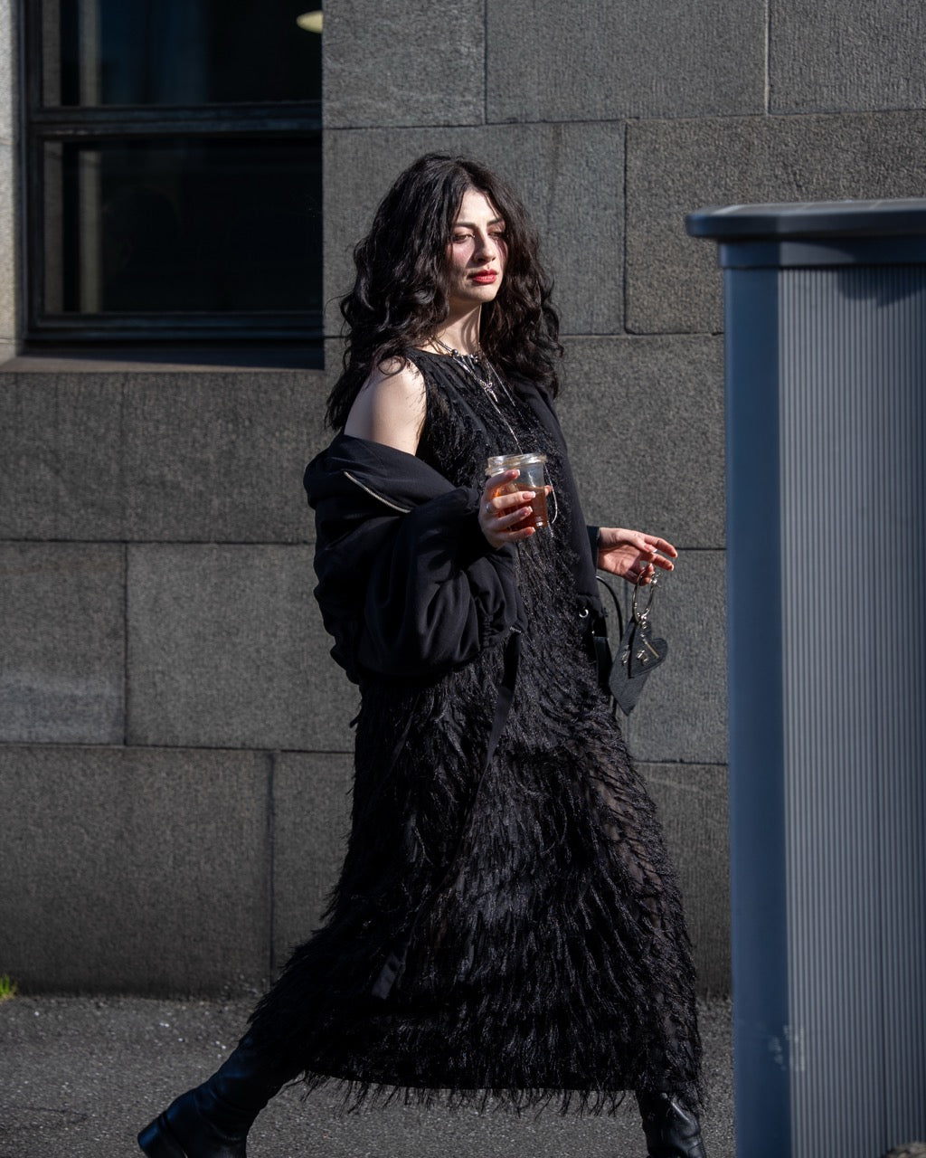 Woman in a black textured dress holding a glass against a gray building background