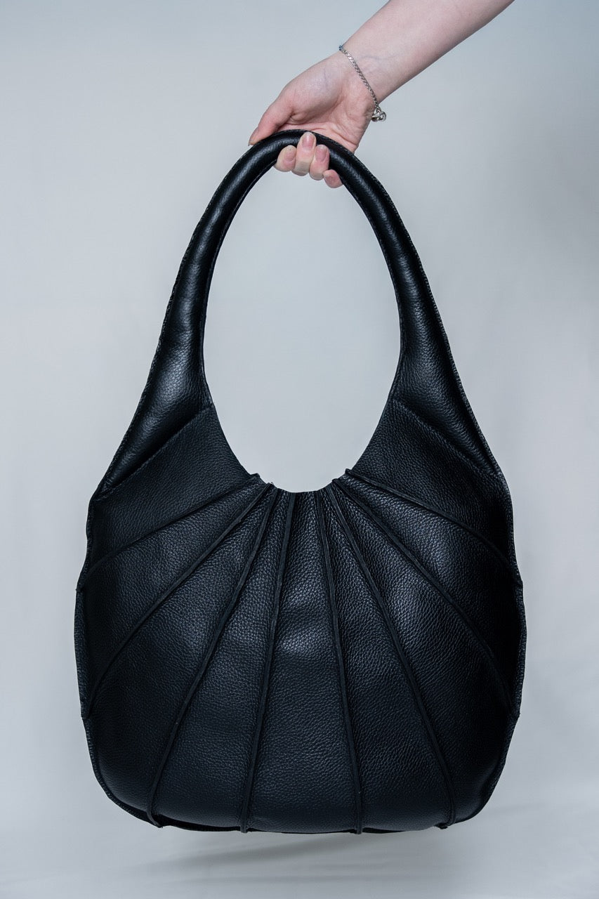 Black handbag held by a person against a light gray background