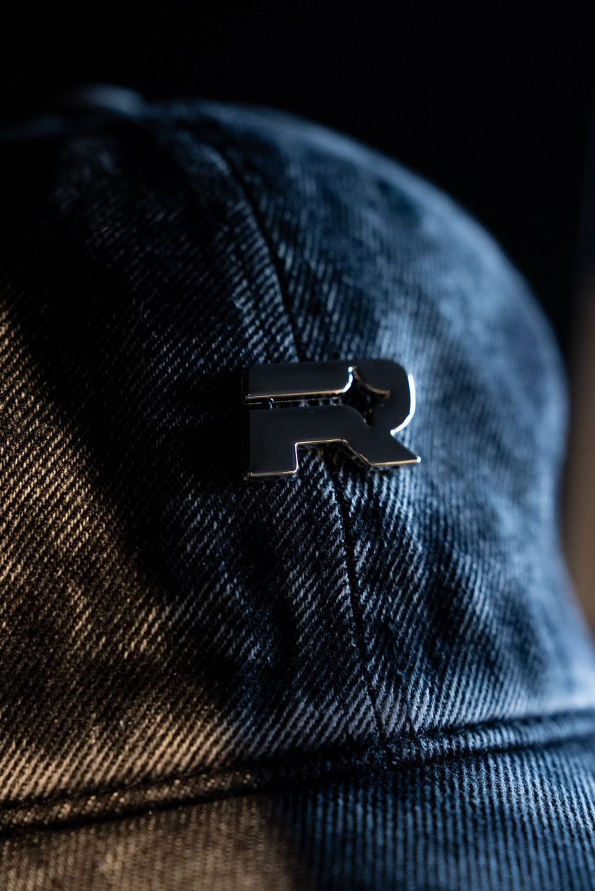 Close-up of a blue denim cap with a black logo on a dark background