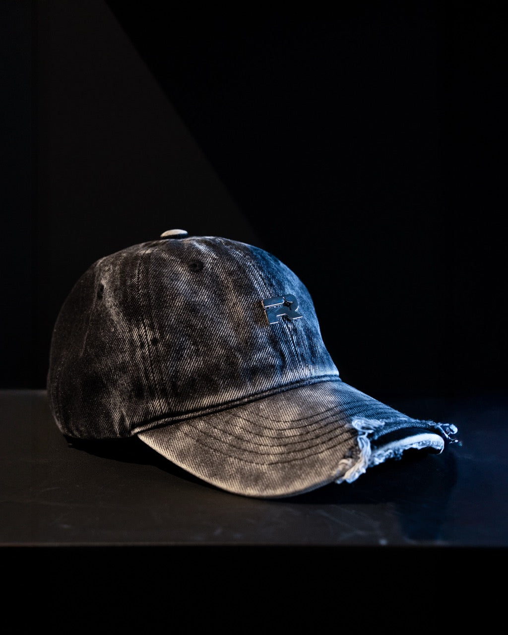 Worn denim cap on a black surface with a dark background