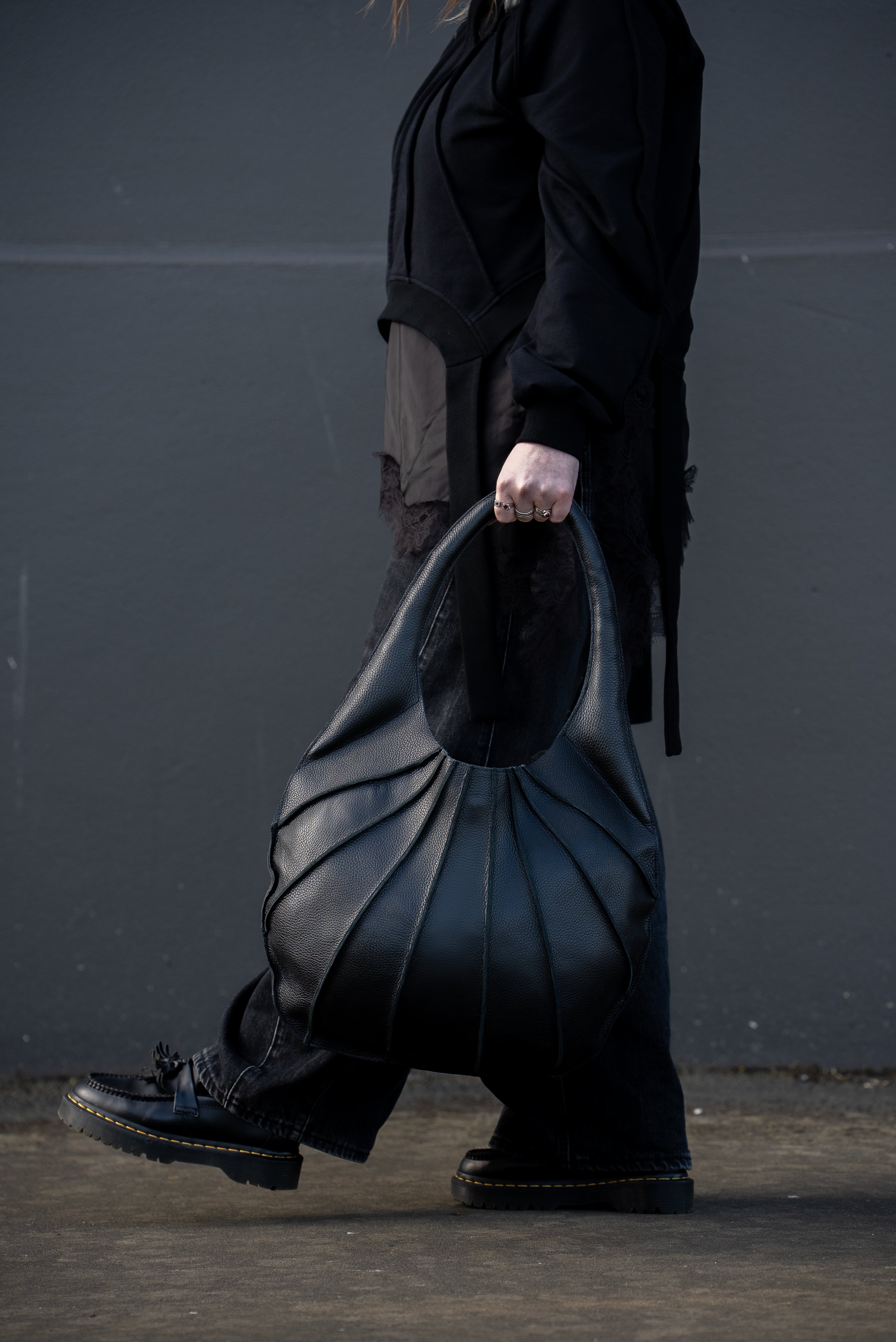 Person holding a large black leather bag against a dark background