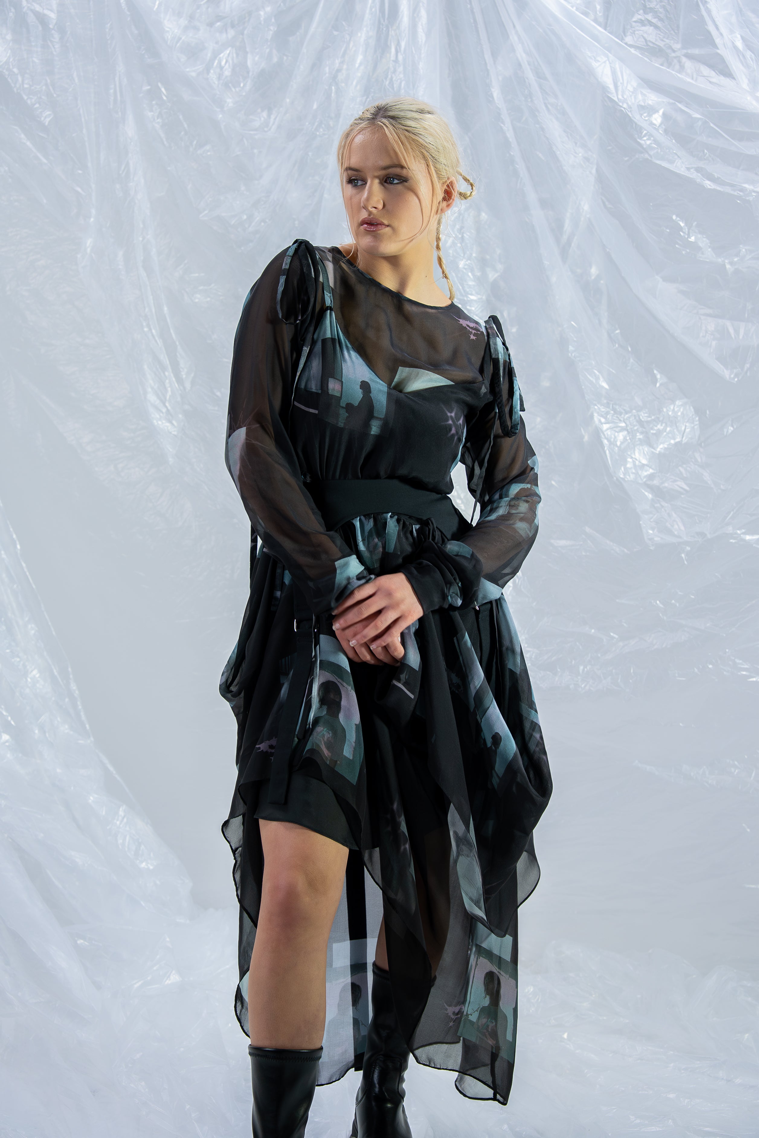 Woman wearing a black and green dress with sheer sleeves against a white background